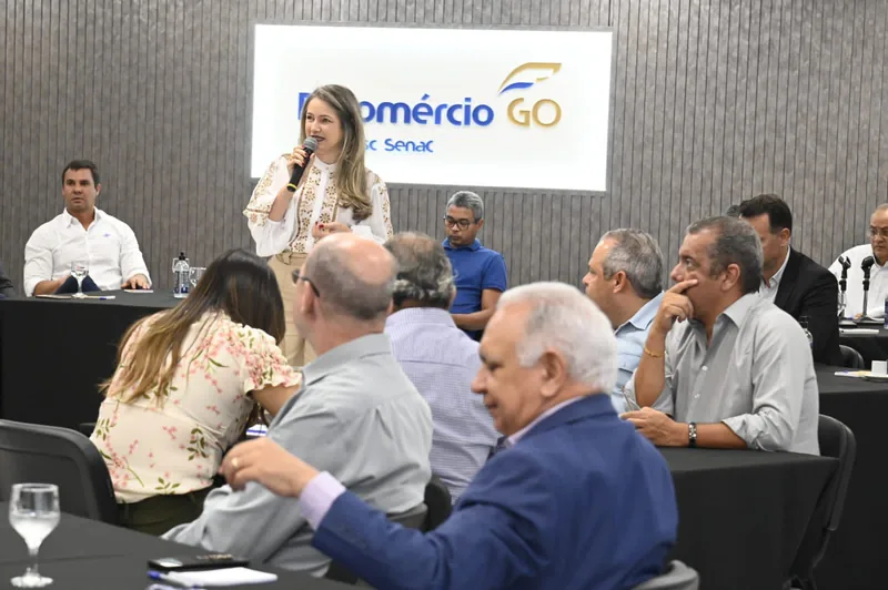 Rejane Duarte falando ao microfone para empresários sentados à mesa, num evento da Fecomércio GO