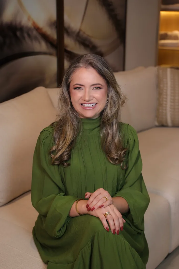Rejane Duarte, sorrindo, de vestido verde, sentada num sofá