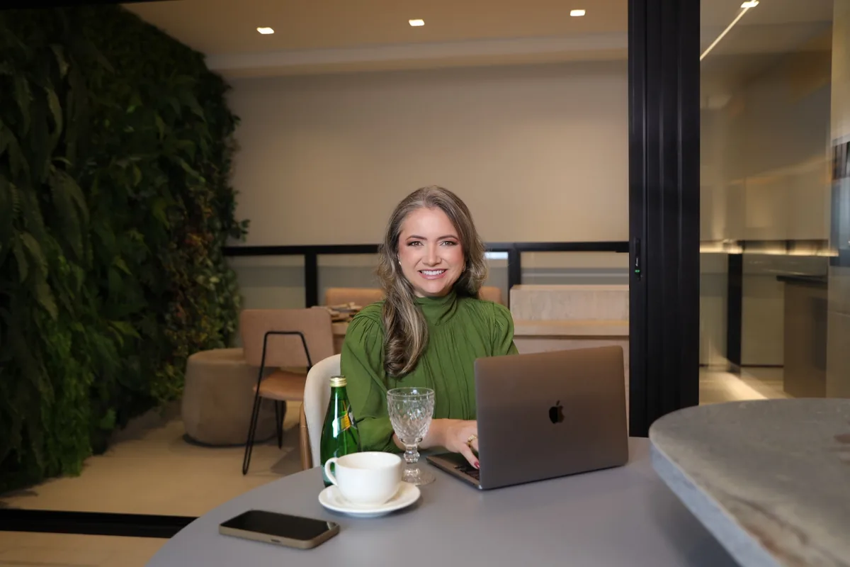 Rejane Duarte sentada à mesa, sorrindo, com o notebook aberto